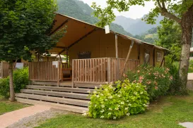 Canvas tent with wooden deck, surrounded by lush greenery and mountains.