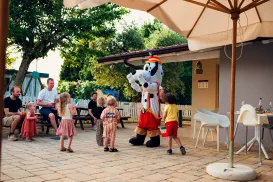 Kids smiling at a costumed character outside under a sunny patio.