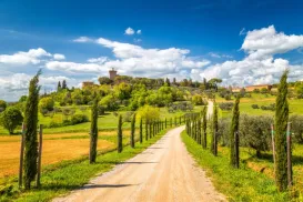 Tuscan countryside with a dirt road, cypress trees, and a scenic hilltop.