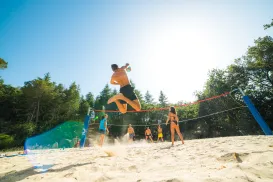 Young adults playing beach volleyball under a sunny sky.