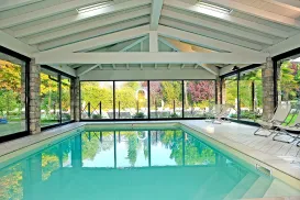 Indoor pool with large windows, surrounded by chairs and colorful trees outside.
