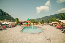 Pool with colorful slides, surrounded by lounge chairs, mountains in the background.