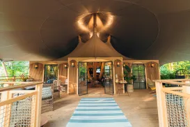 Open-air tent with striped rug, warm lights, and wooden furniture.
