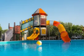 Playground with colorful slides by a pool under a clear blue sky.