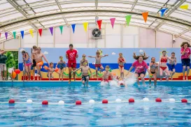 Children joyfully jumping into an indoor pool under colorful bunting.