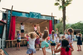Children dancing in front of an outdoor stage with red curtains.