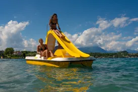 Pedalo with yellow slide on a lake under a blue sky.