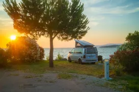 Camper van parked by a lake at sunset, surrounded by trees and bushes.