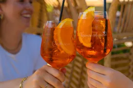 Toasting with orange drinks on a sunny day, woman smiling in the background.