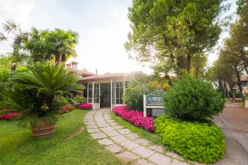 Lush garden path leading to a cottage, surrounded by vibrant flowers and tall trees.