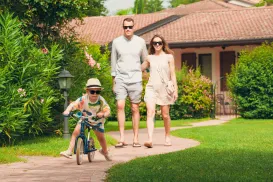 Child on a bike with adults walking behind in a garden setting.