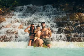 Family posing in front of a waterfall in swimwear.