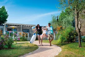 Family walking on a garden path, carrying beach gear, sunny day.
