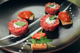 Gourmet tartare dish with basil and cream garnishes on a dark plate.