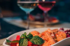 Salad with salmon and basil in a white dish, two wine glasses in the background.