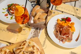 Dining table with Aperol spritz, bread, bruschetta, prosciutto, and melon.