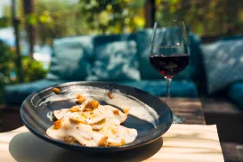 Pasta with creamy sauce and a glass of red wine on an outdoor table.
