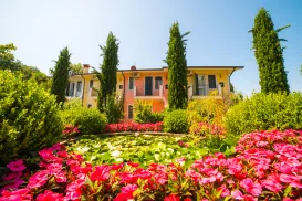 Colorful house with lush garden, pink flowers, and tall trees under a blue sky.