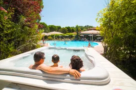 Family relaxing in a hot tub by a sunny outdoor pool.