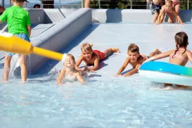 Children playing in a shallow pool with a water gun and float tube.