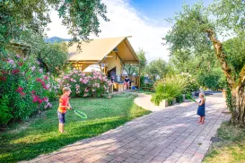 Children playing on a path near a garden and tent under a bright blue sky.