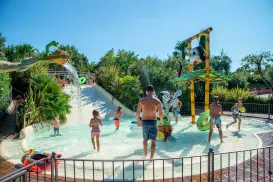 Water park splash zone with kids and adults playing, bright sunny day.