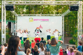 Children watching a stage performance with dancers and a dog mascot.