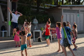 Children dancing energetically outdoors near a wooden building.