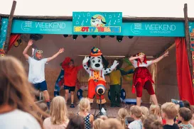 Children watching a colorful stage performance with a mascot in costume.