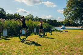 People exercising on elliptical machines outdoors by a lake.