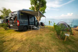 Camper van and tent on grassy shore with ocean view.