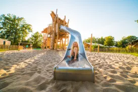 Child on a playground slide in a sunny park.