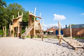 Wooden playground on sand, sunny day, scattered clouds in blue sky.