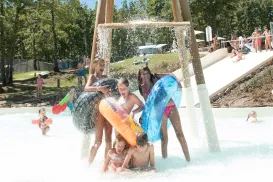 Children playing under a water spray feature in a sunny park.