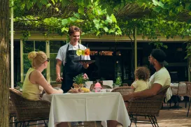 Waiter serving drinks to a family at an outdoor restaurant table.