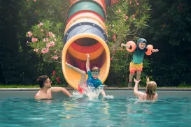 Family playing in a pool, children jumping from a colorful slide.