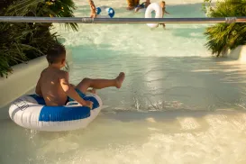 Child on a water slide in an inner tube, splashing into a pool.