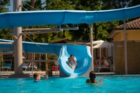Kids playing in a pool with a blue waterslide on a sunny day.