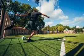 Man kicking soccer ball on outdoor field, blue sky above.