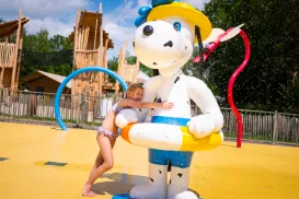 Child hugs large Snoopy statue at colorful water park.