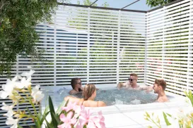 Four people relaxing in a hot tub surrounded by white privacy screens and flowers.