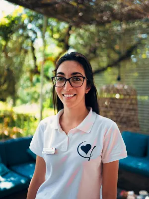 Smiling woman in a white shirt with glasses, standing outdoors.