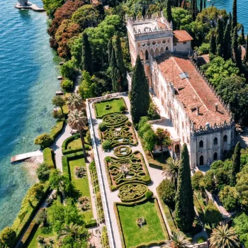 Aerial view of a lakeside villa with intricate gardens and lush greenery.