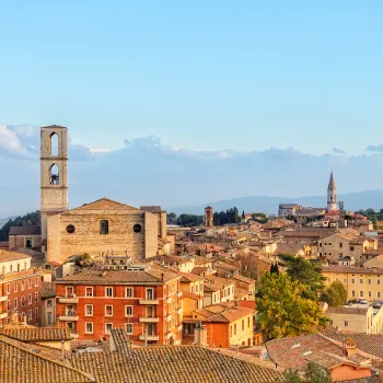 Rooftop view of a historic European city with bell tower and distant hills.