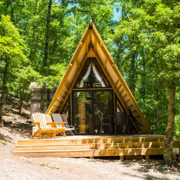 A-frame cabin in a forest, with a small deck and chairs.