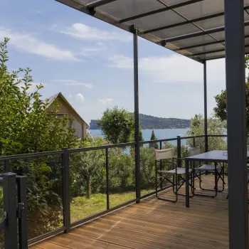 Covered patio with table, overlooking lush greenery and a distant lake under a blue sky.