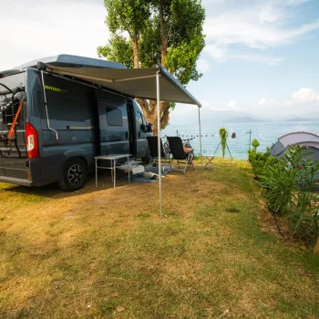 Campervan and tent on grassy lakeside campsite under clear blue sky.