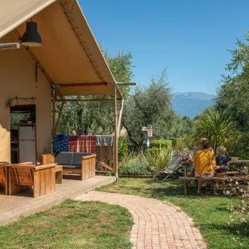 Tent with patio in sunny garden, group seated at table, distant mountains.
