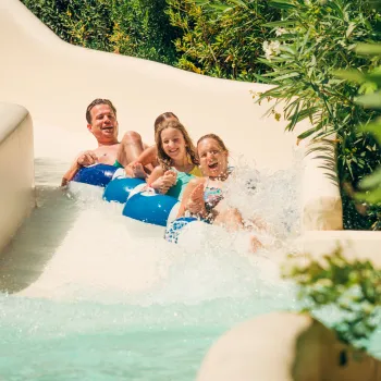 Group of people on a water slide, smiling and splashing.