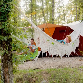 Two people relaxing at a campsite in a hammock under trees.